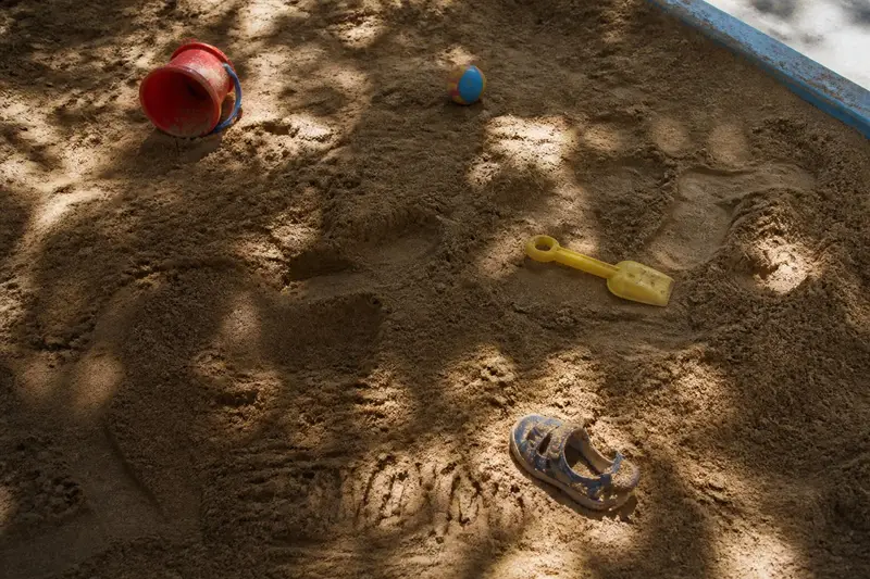 ארגז חול בחצר גן ילדים, מצולם מלמעלה: דלי ואת פלסטיק, כדור קטן וסנדל ילדים אחד שנשאר בחול