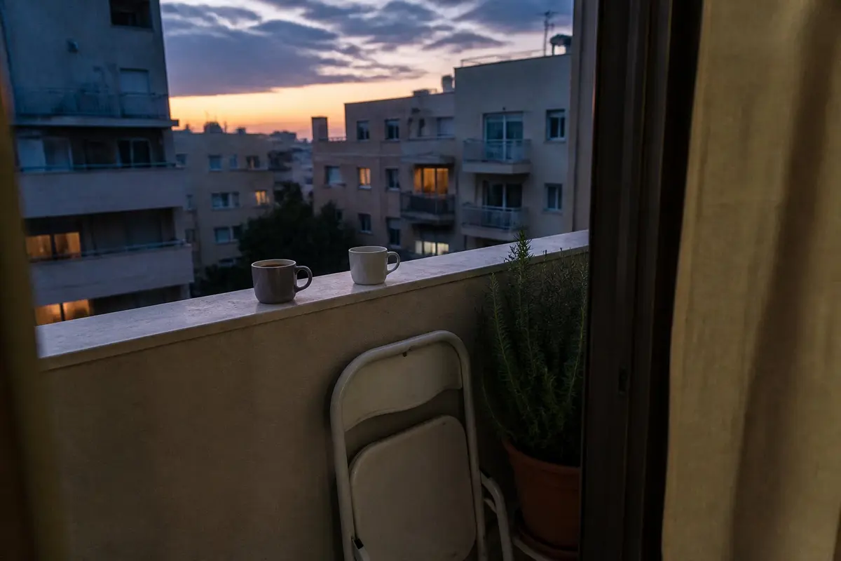 שתי כוסות, שתי גרסאות של אותו ערב. ברוב הזוגות זה פשוט חלק מהחיים יחד. שתי כוסות קפה על מעקה מרפסת בדמדומים, אחת מלאה ואחת ריקה, עם כיסא פלסטיק מקופל ועציץ רוזמרין