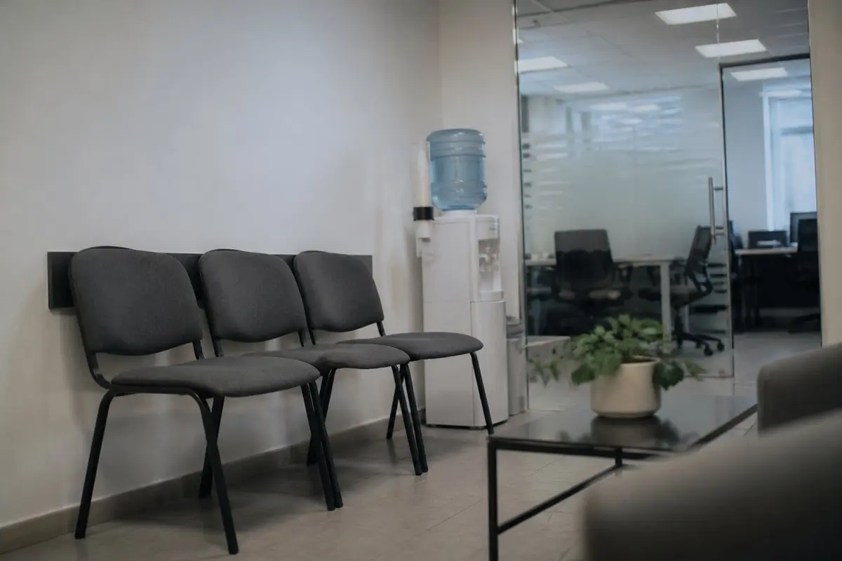 ההמתנה לפני הראיון קצרה בדרך כלל ממה שהיא מרגישה, וזה זמן טוב לנשימה אחת ארוכה. פינת המתנה במשרד: שלושה כיסאות אפורים ליד קיר לבן, מתקן מים, שולחן נמוך עם עציץ וקיר זכוכית של חדר ישיבות