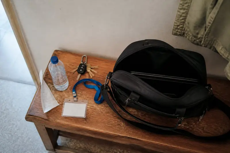 ספסל עץ בכניסה לדירה, ועליו תיק מחשב פתוח, תג עובד על שרוך כחול, צרור מפתחות, בקבוק מים וקבלה מקומטת